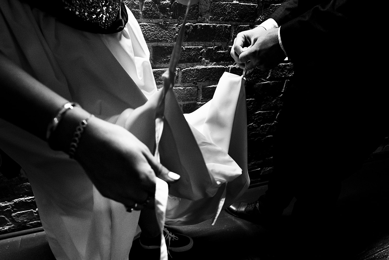 Groom helps bride bustle her dress - focus is on their hands and the ties