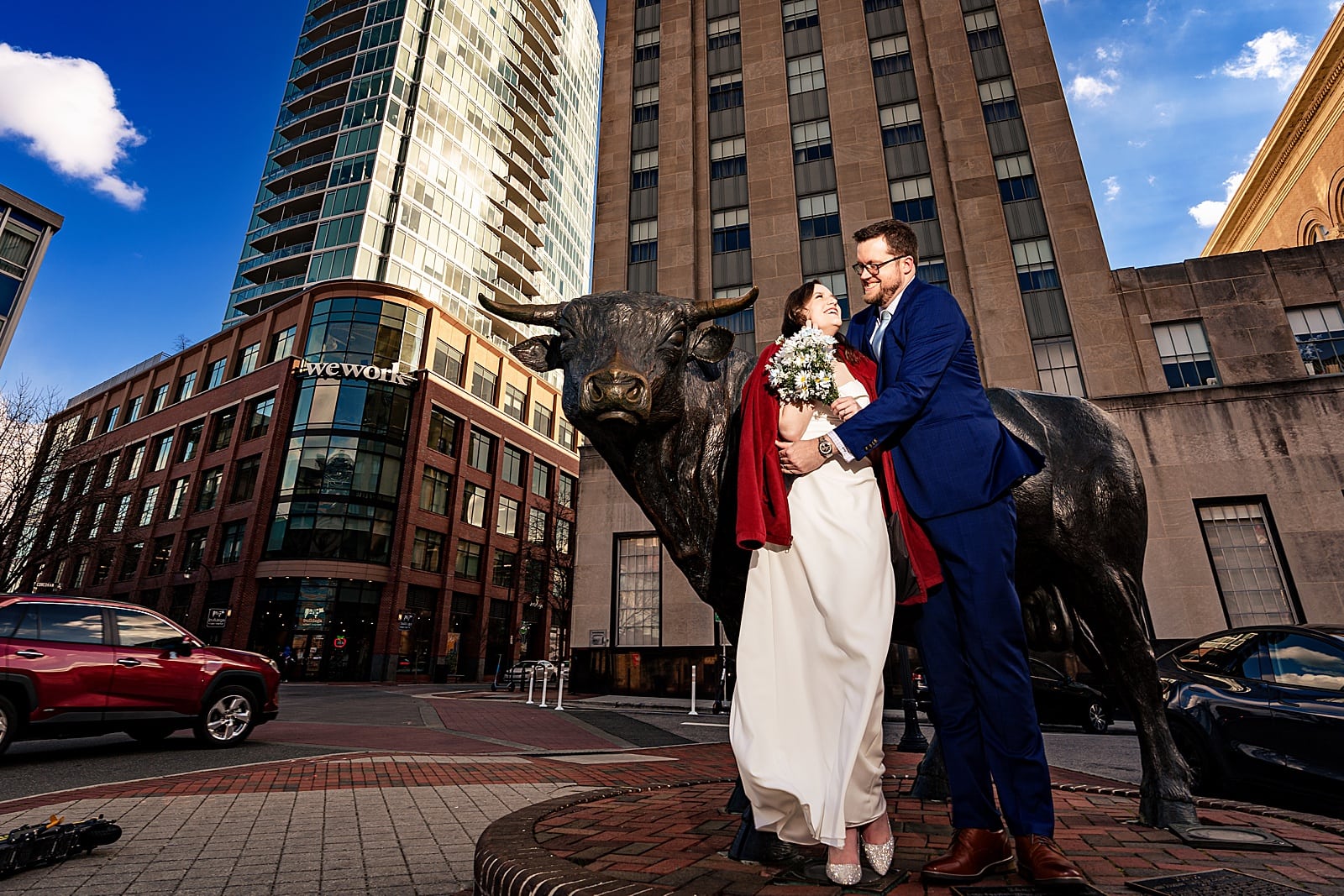 A bride snuggles in the grooms coat to stay warm on their chilly wedding day in downtown Durham, NC