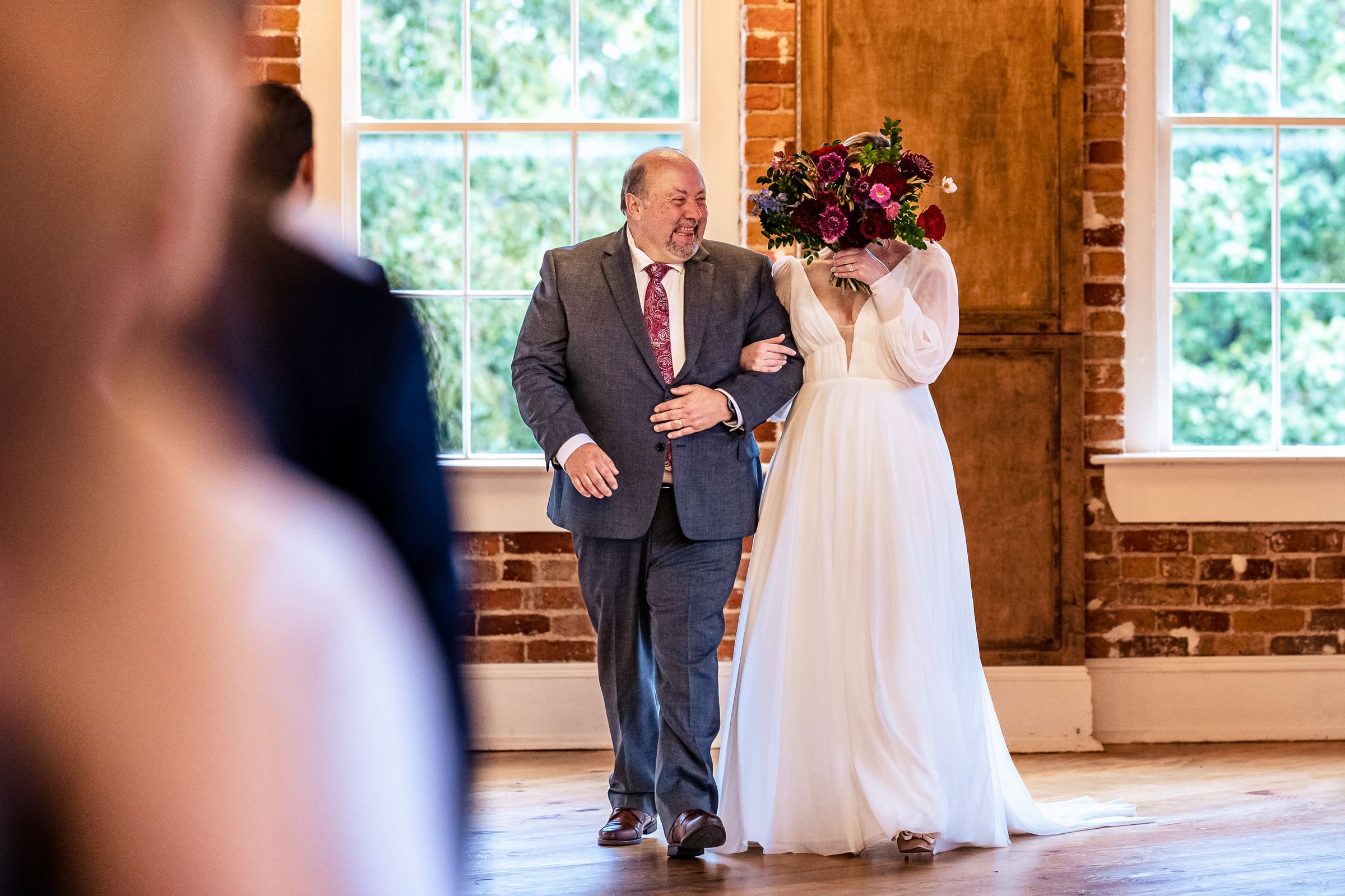 bride hides her face behind her bouquet as she laughs and cries walking down the aisle | photos by Kivus & Camera