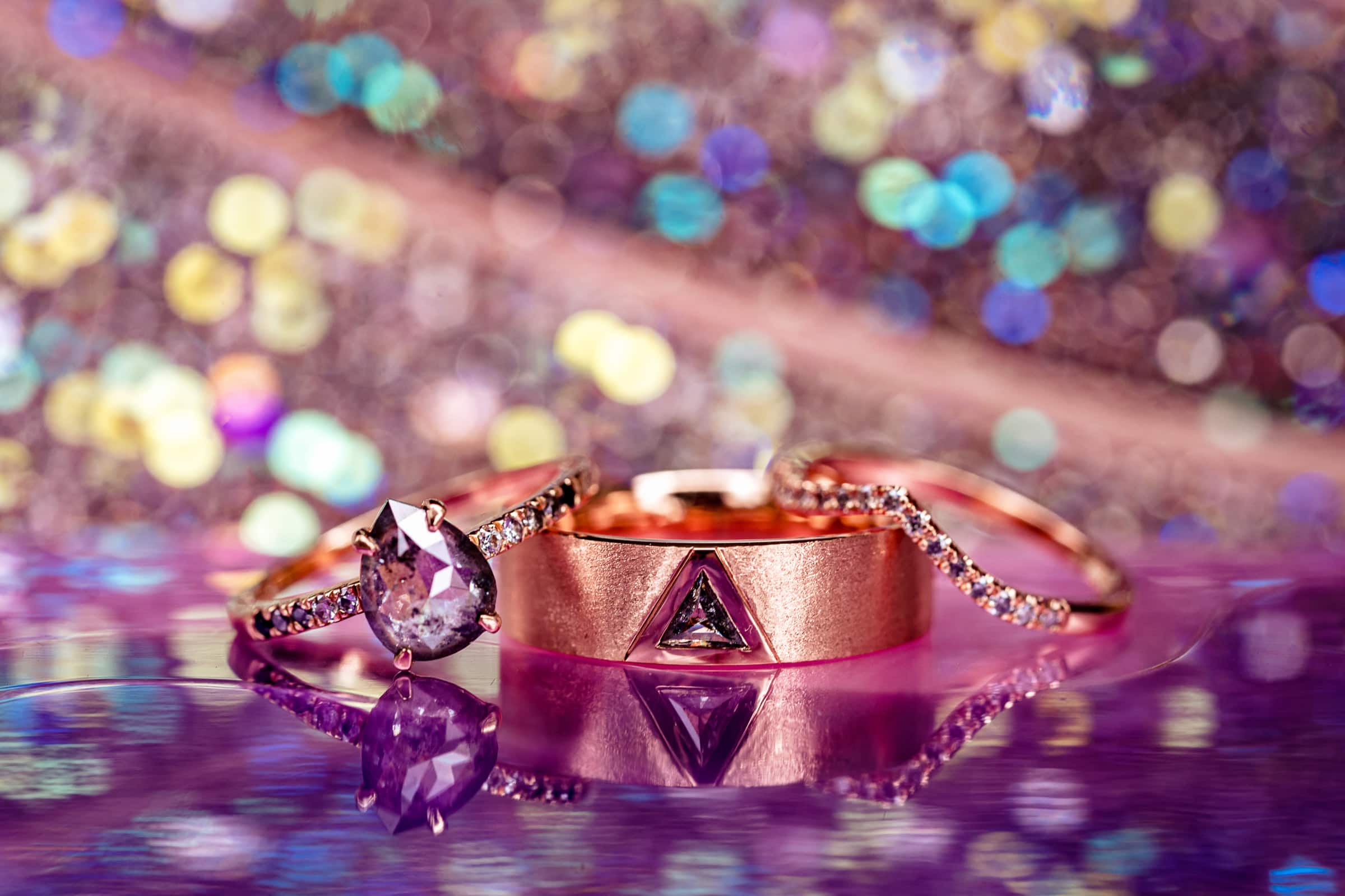 unique, artistic wedding rings on a glossy purple surface with pink and purple glittery background | Kivus & Camera