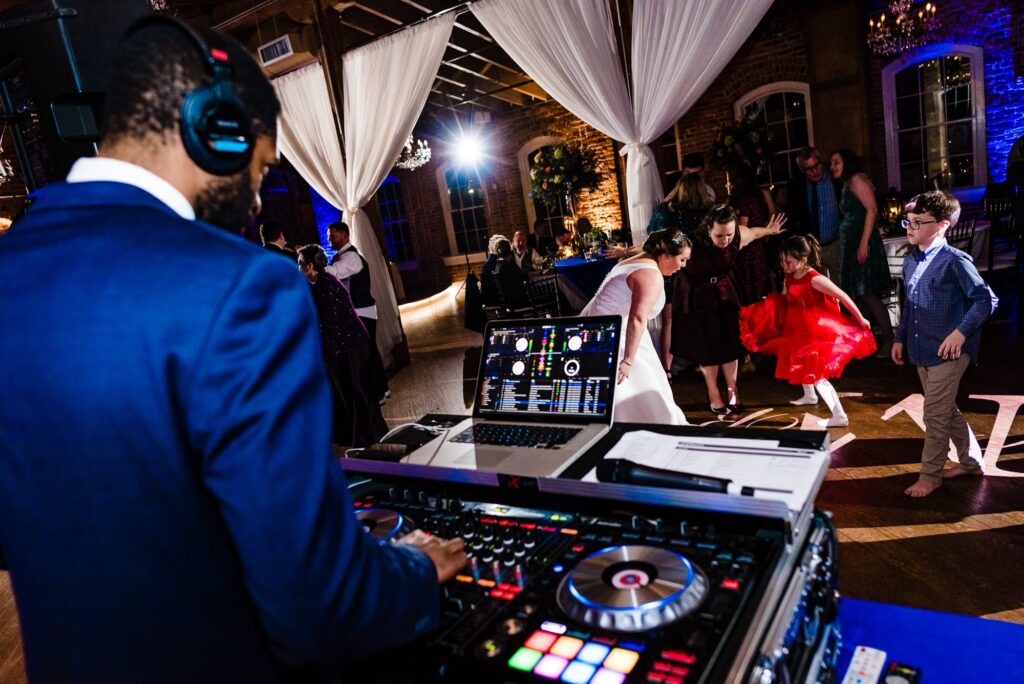 Photo from behind a SPIN DJ booth shows the turntables and people dancing at the wedding reception. | photo by Kivus & Camera