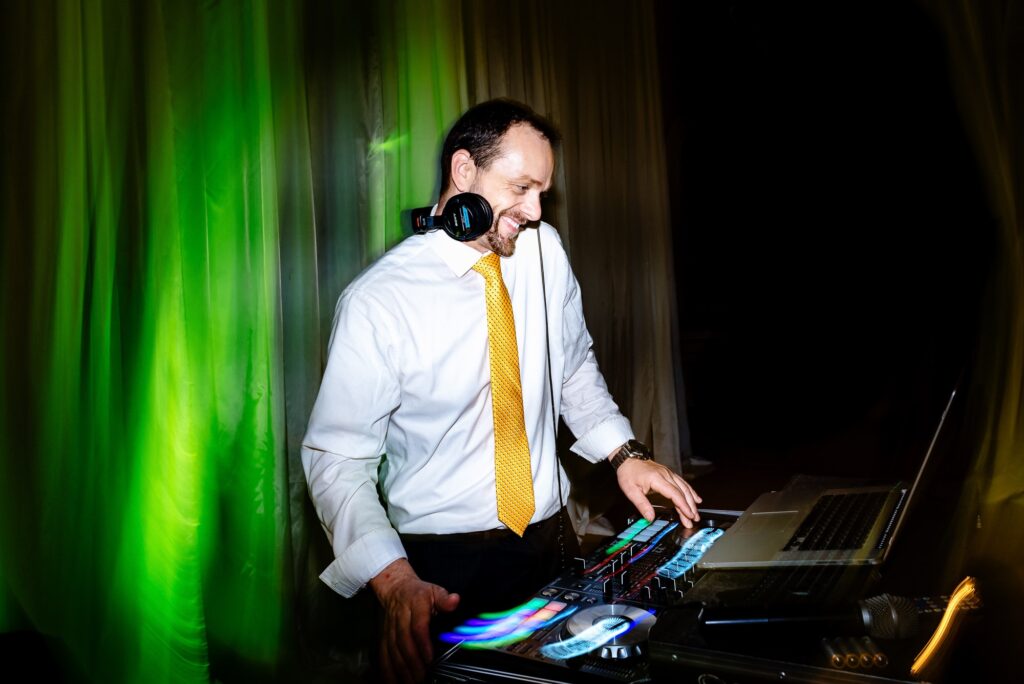 Eric from All Around Raleigh DJs smiles behind his DJ booth at a wedding | photo by Kivus & Camera