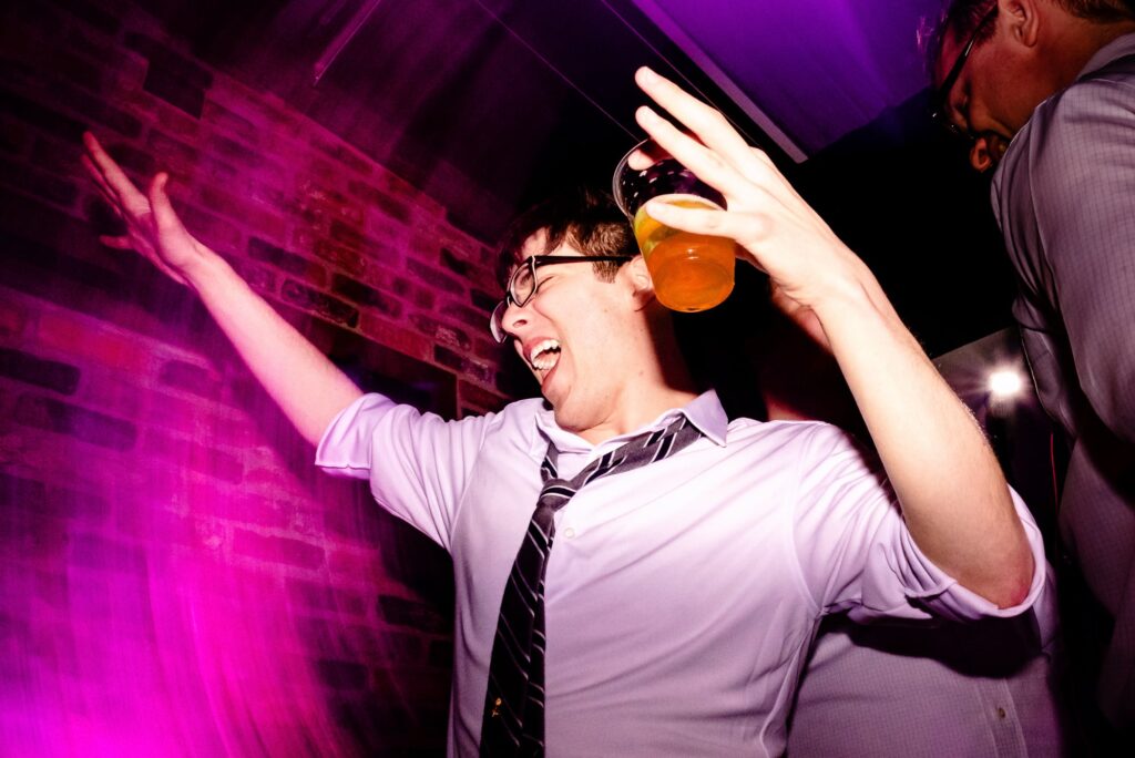man with a beer in his hand dances at a wedding with bright pink and purple uplighting all around him | photo by Kivus & Camera