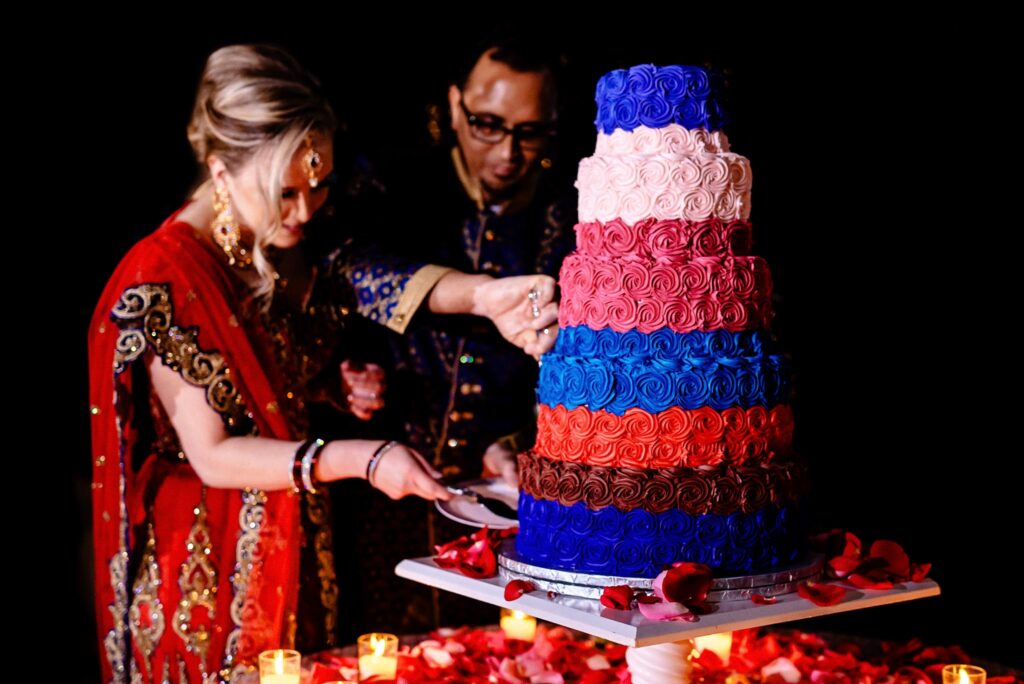 couple in Indian wedding attire slices into a colorful 5 tier wedding cake | photo by Kivus & Camera