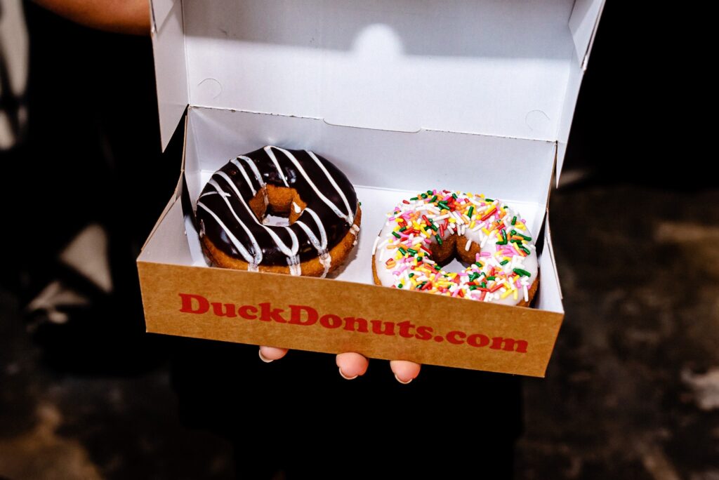 two frosted and decorated donuts in a to-go box as a wedding favor | photo BY Kivus & Camera