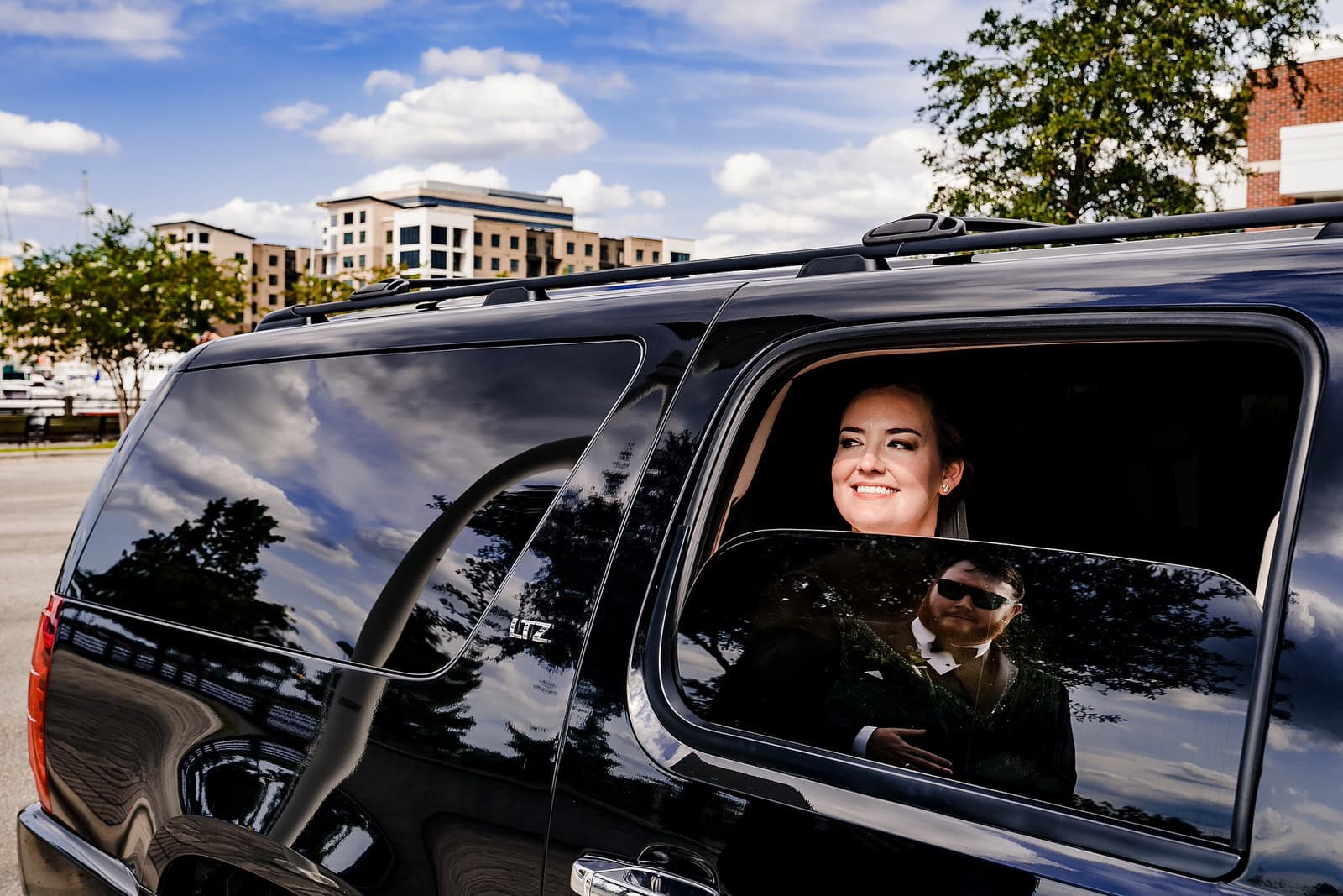A bride looks out the window of the getaway car; the groom is reflected in the window