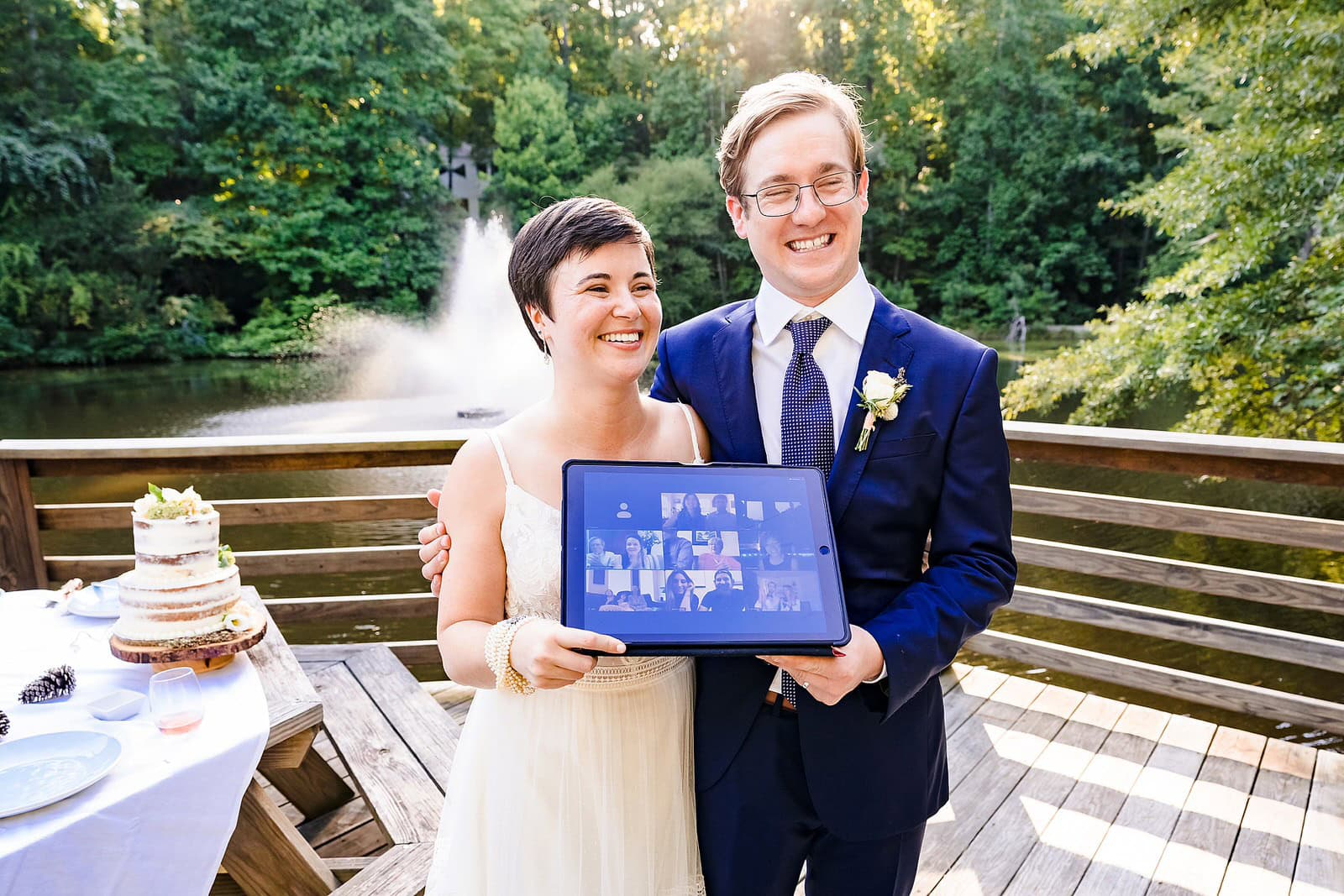 wedding couple pose with an ipad showing just a few of the guests who were in attendance at their micro-wedding via zoom