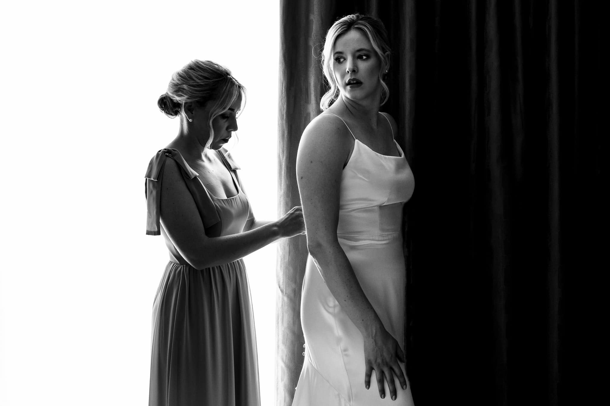 maid of honor zips bride into her Alexandra Grecco wedding dress | photo by Kivus & Camera