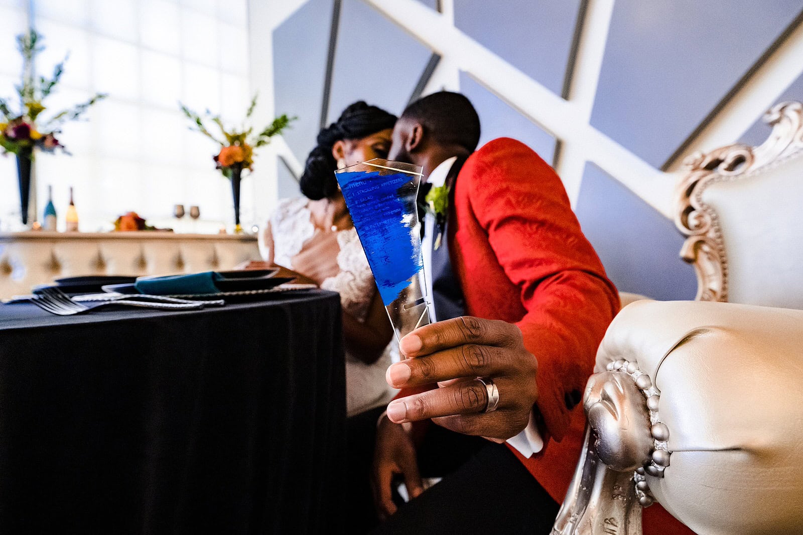 Groom holds out wedding menu as he and bride kiss at sweetheart table