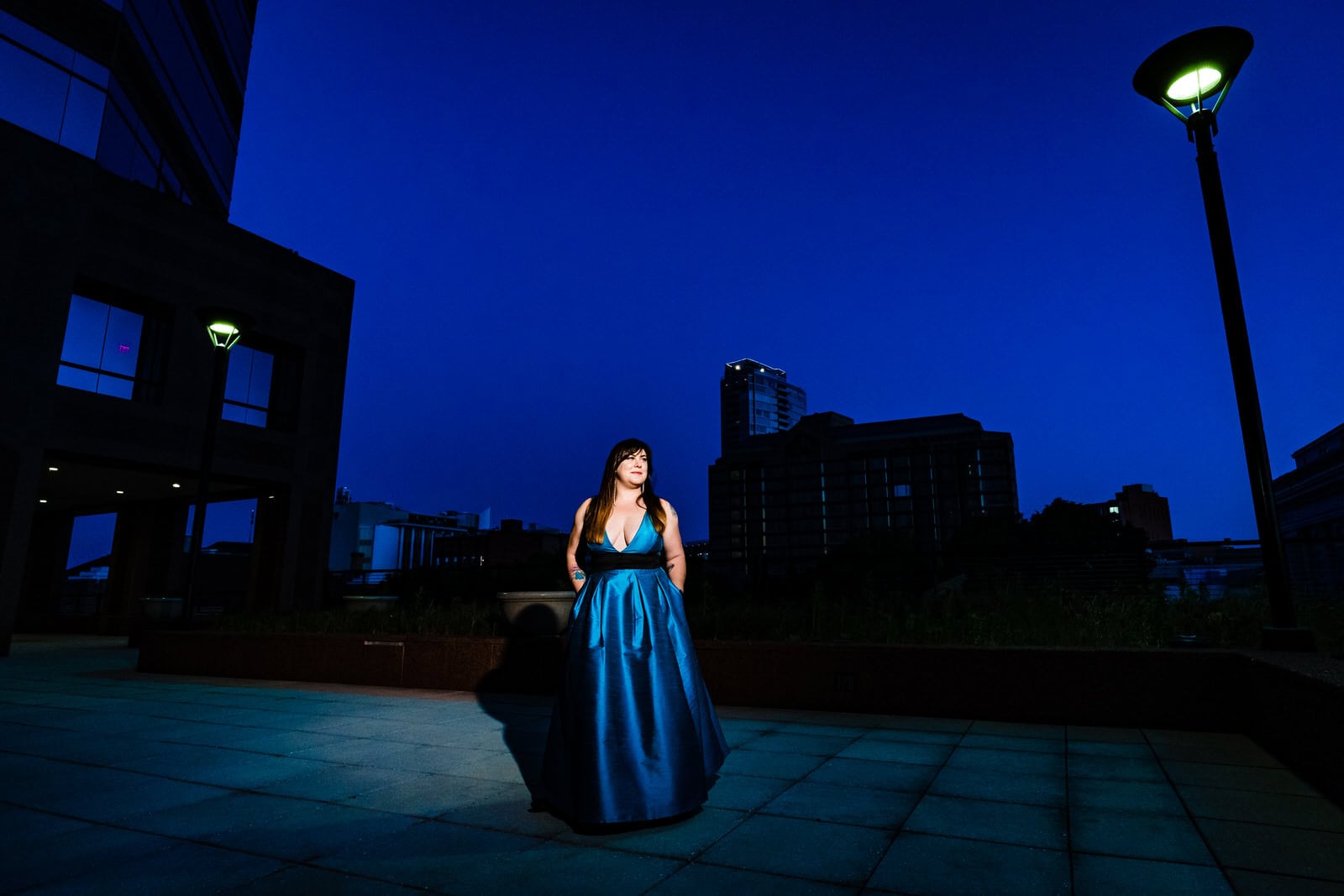 Woman in a teal dress poses on a rooftop in front of the Durham skyline and a deep blue sky