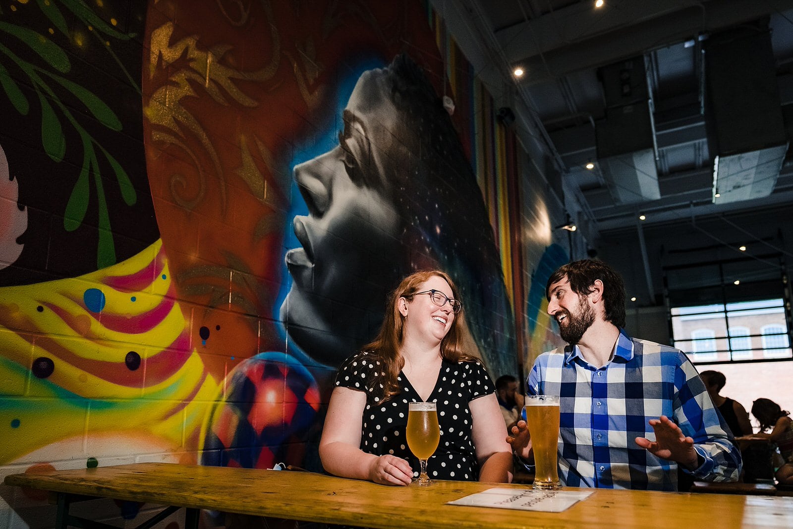 A man and a woman laugh with beers at Durham Brewery Hi-Wire, during their engagement session