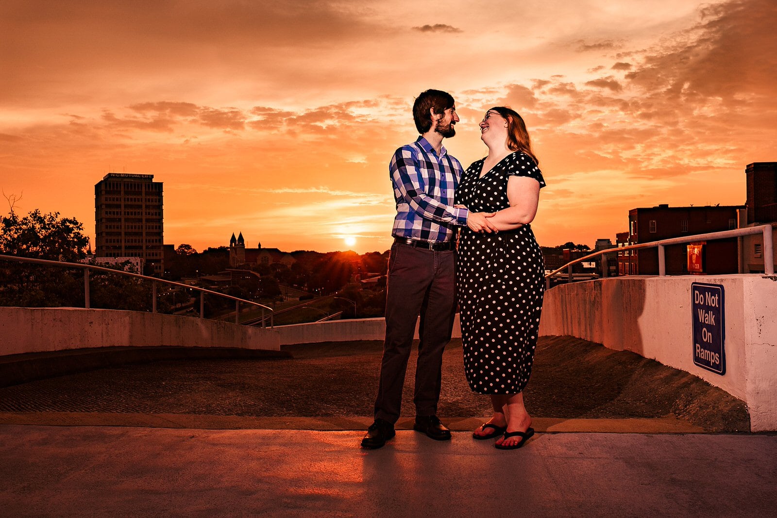 A couple embraces in front of the backdrop of an orange sunset