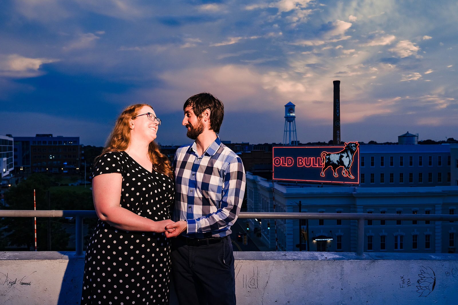 Engaged couple smiles in front of the Bull Durham mural at American Tobacco Campus