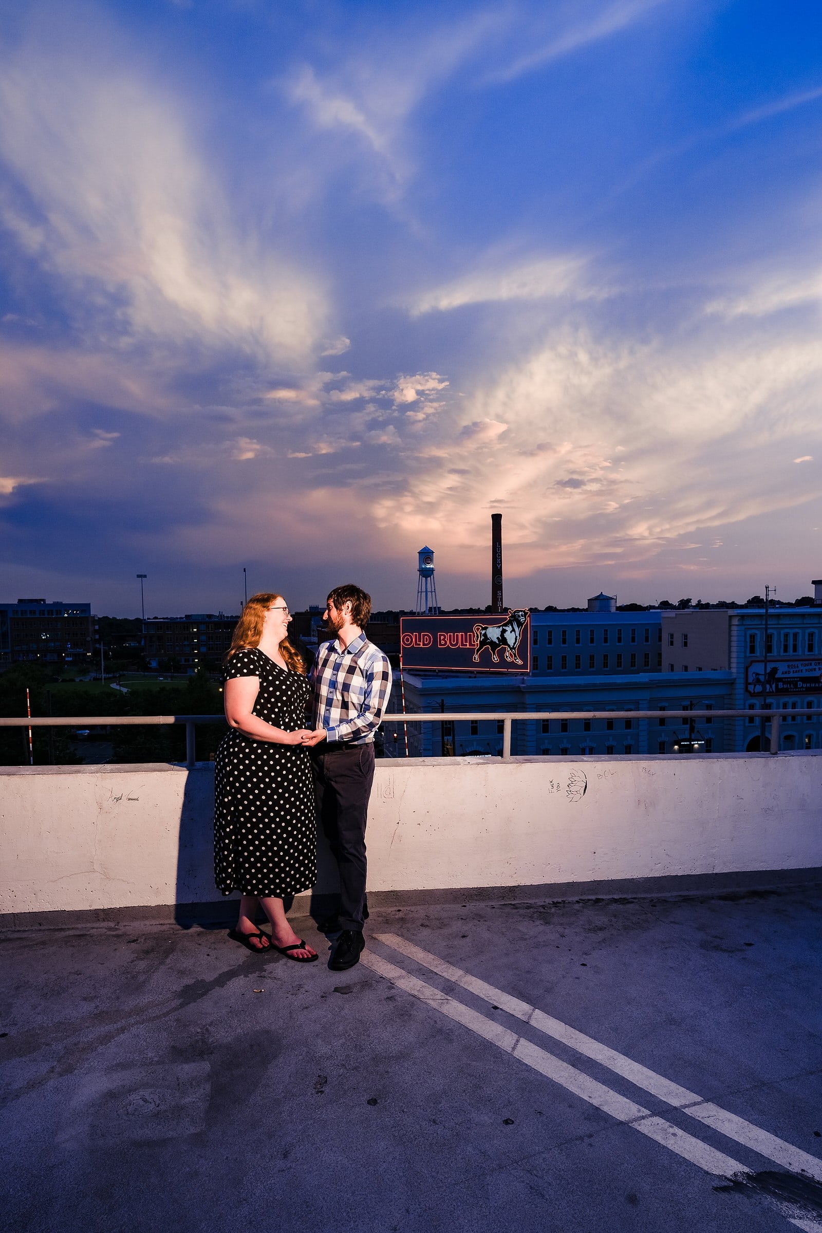 Engaged couple smiles in front of the Bull Durham mural at American Tobacco Campus
