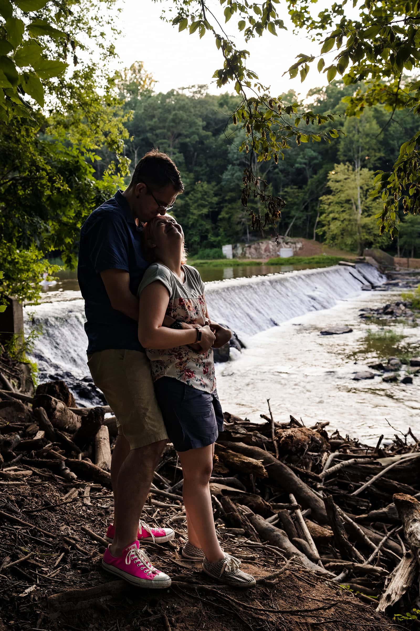 a man and a woman embrace at the Eno River for their engagement photos