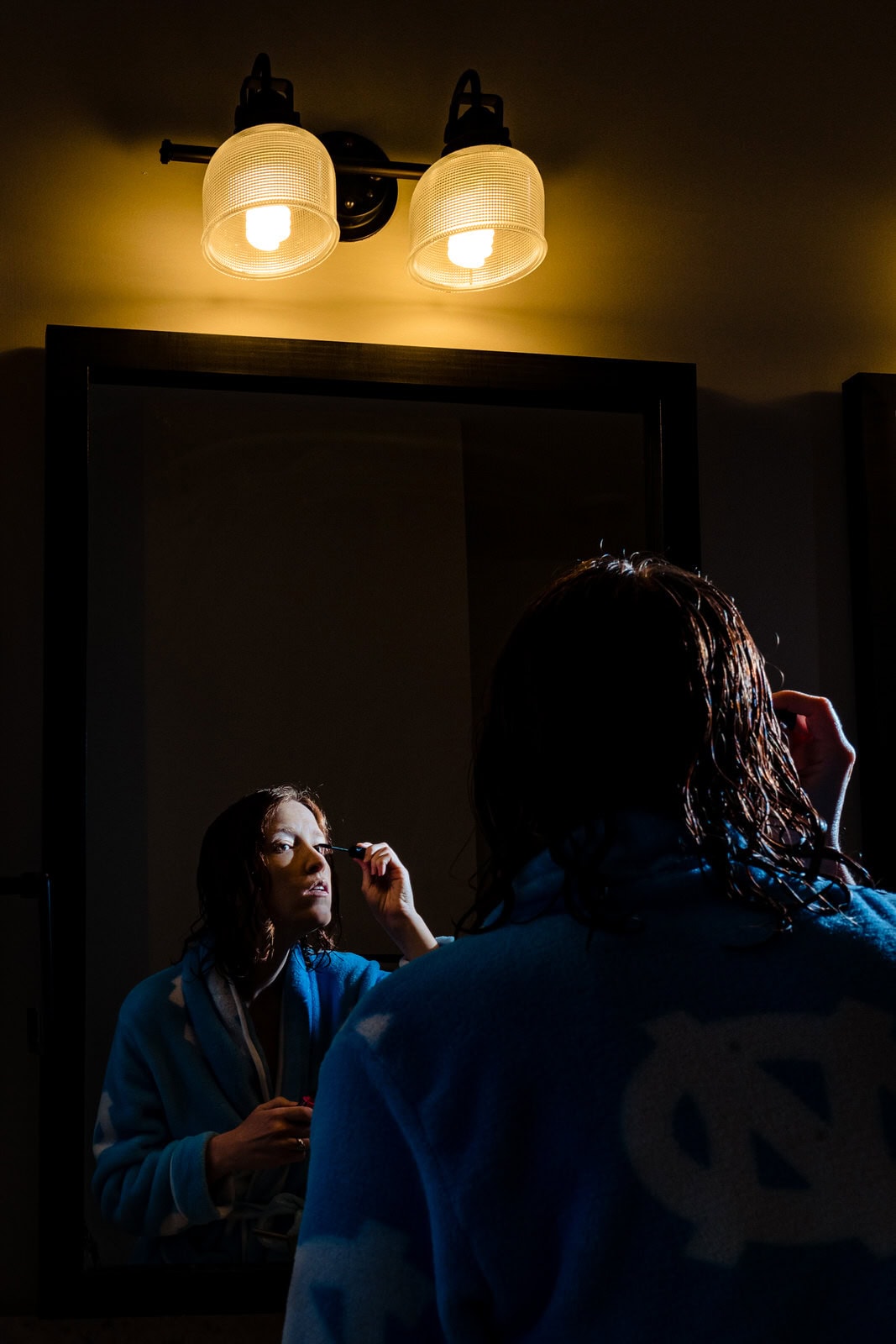 during a fake quarantine wedding, bride puts mascara on while looking in the mirror