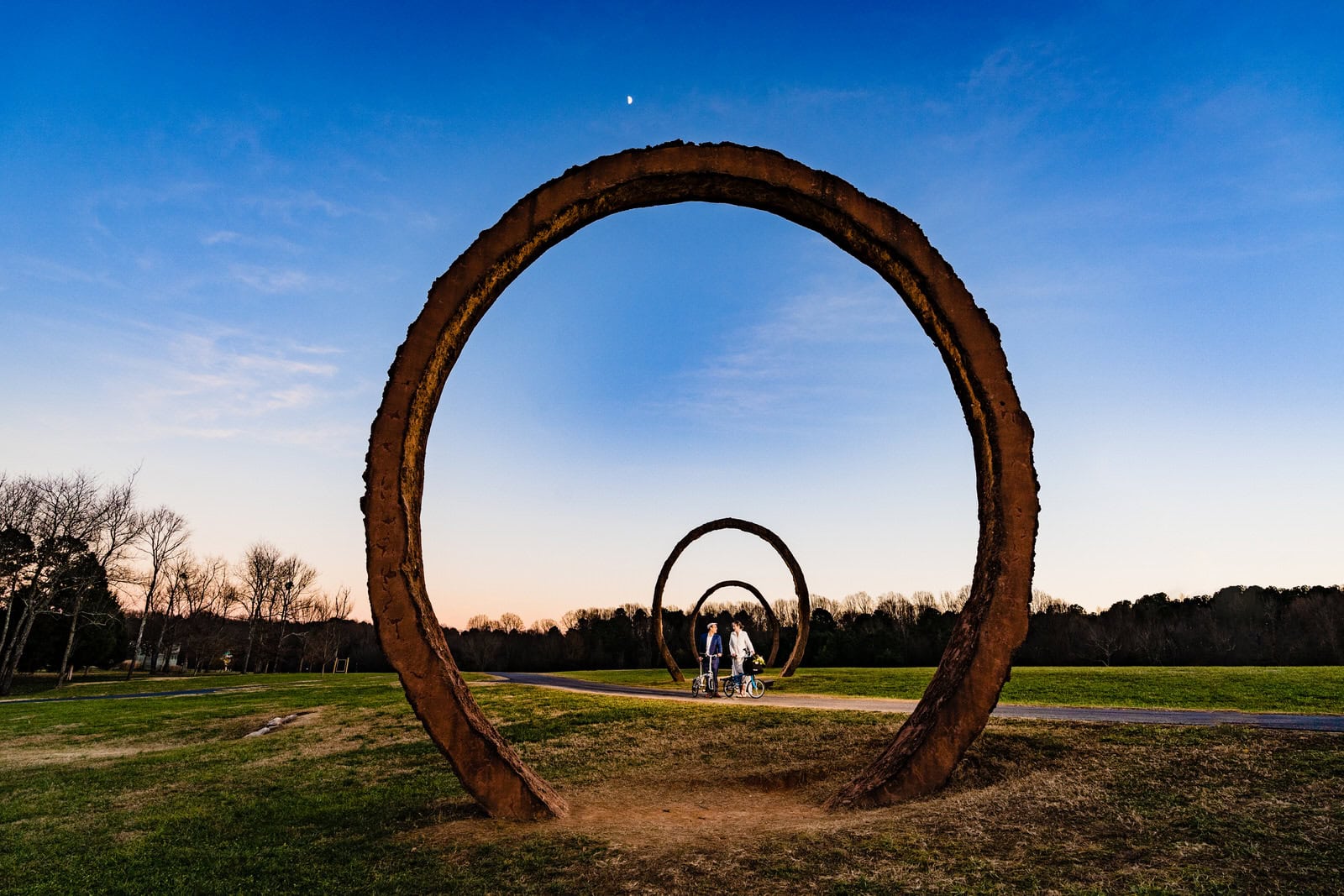 bride and groom ride through the North Carolina Museum of Art on their bicycles after their winter elopement