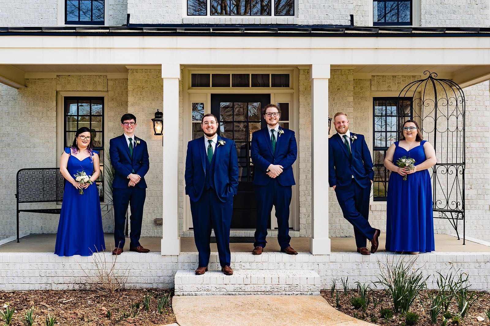 Groom and his attendants pose for a portrait by Raleigh wedding photographers at The Meadows Raleigh. They wear blue suits and blue dresses. 
