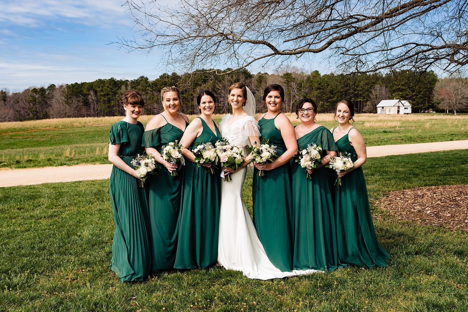 Bride and her bridesmaids pose for portraits by Raleigh wedding photographer at The Meadows Raleigh. The bridesmaids wear green dresses. 