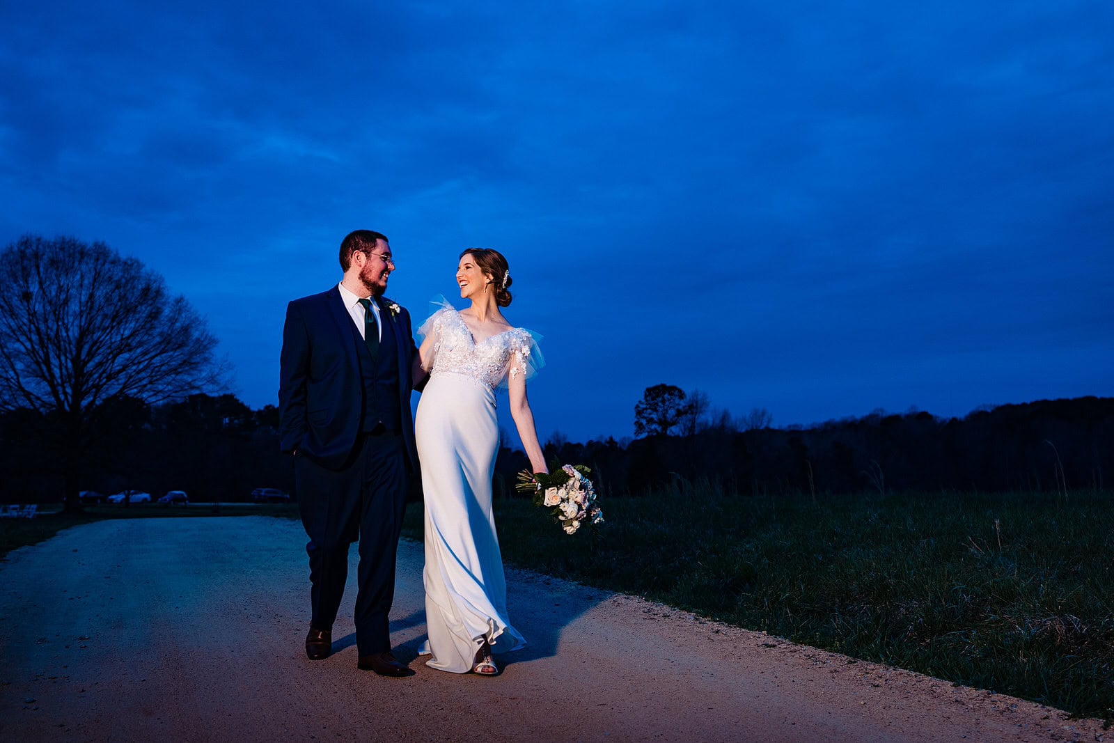 Bride and groom laugh and walk along the road at their wedding at The Meadows Raleigh
