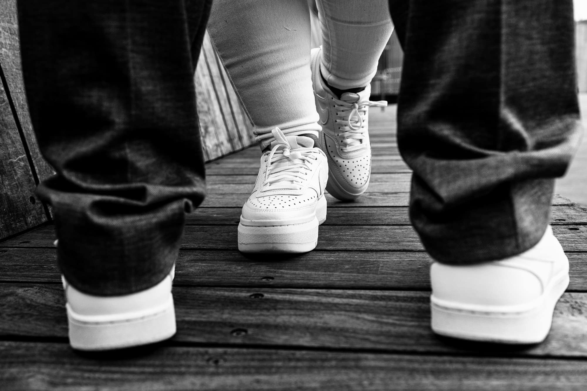 two pairs of feet, both in white sneakers