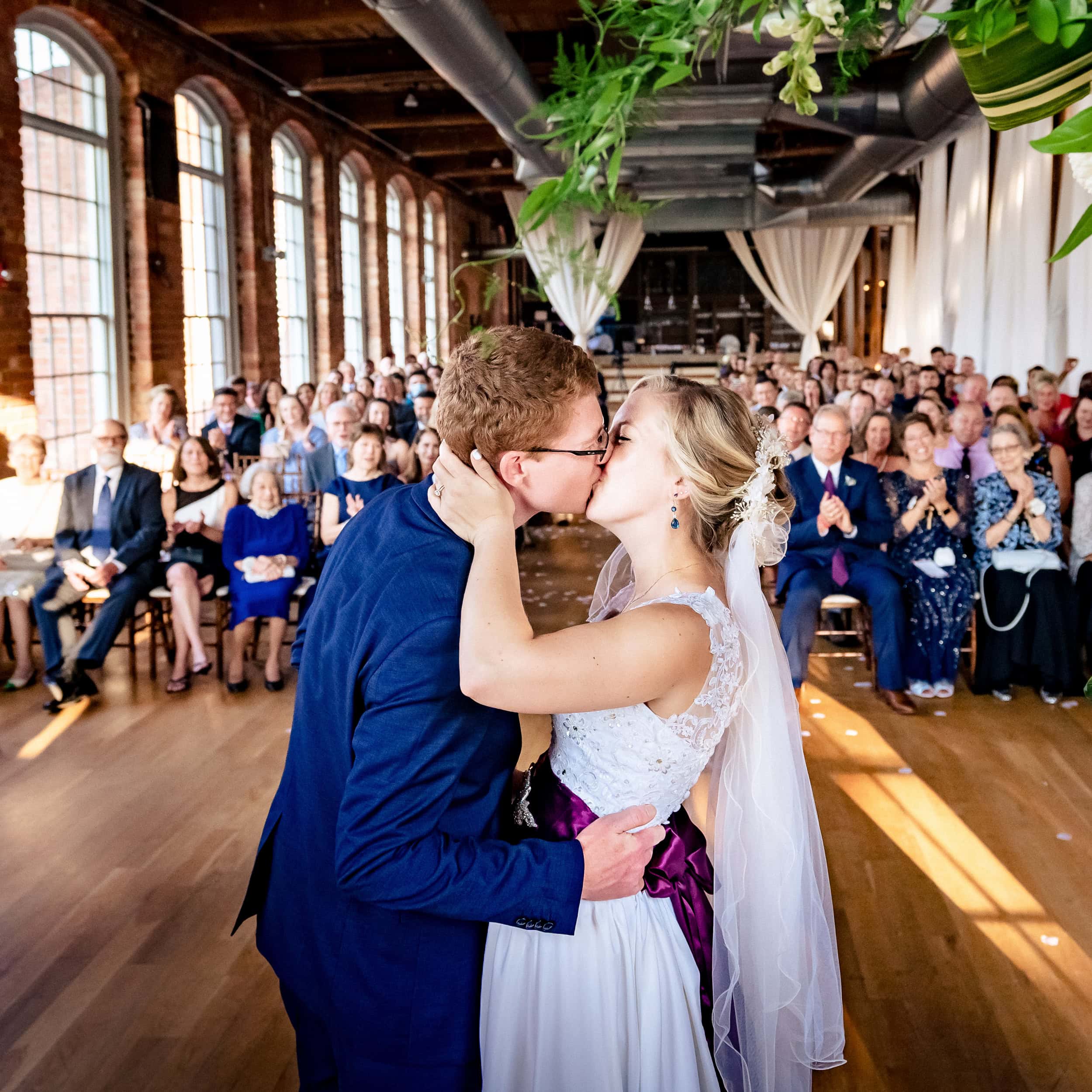 Couple in wedding attire shares their first kiss at The Cotton Room | photo by Kivus & Camera