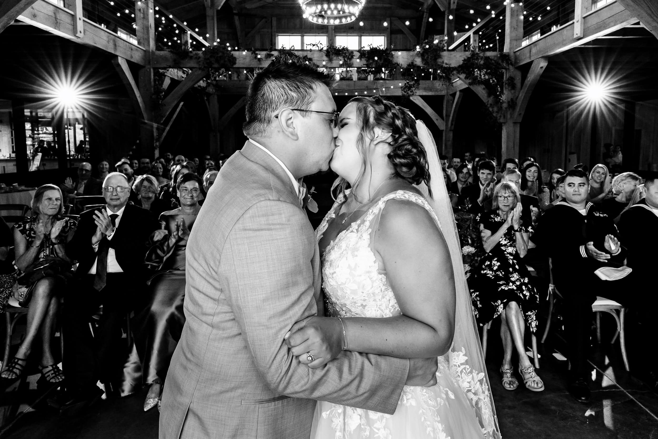 Bride and groom share their first kiss with their friends and family in the background