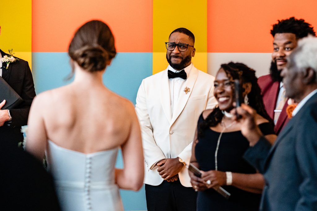 groom holds back tears as he reacts to bride walking down the aisle toward him