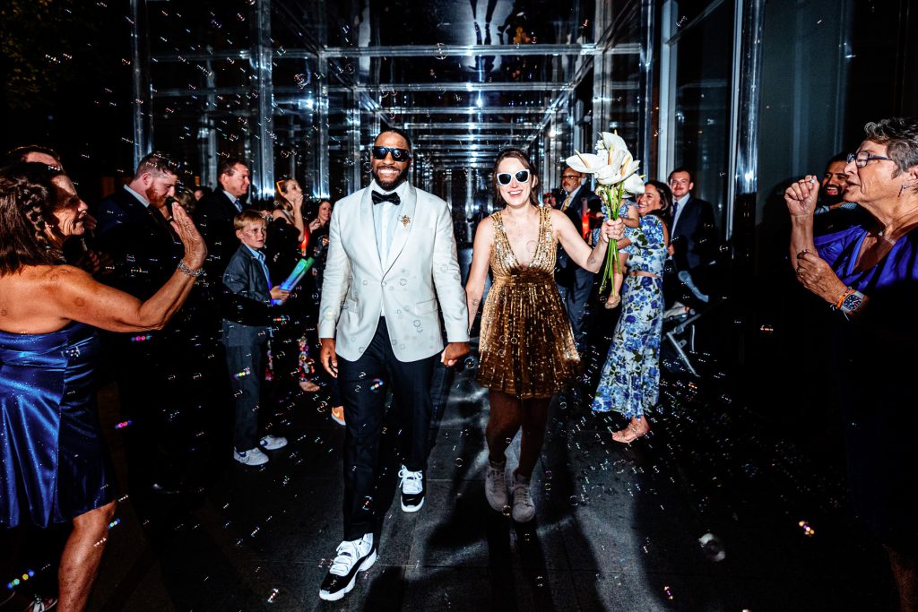 wedding couple exits their reception through a mirrored passage as guests blow bubbles toward them