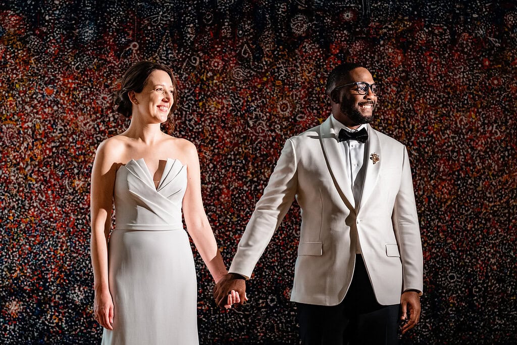 couple in wedding attire poses for a portrait with art behind them during their North Carolina Museum of Art wedding