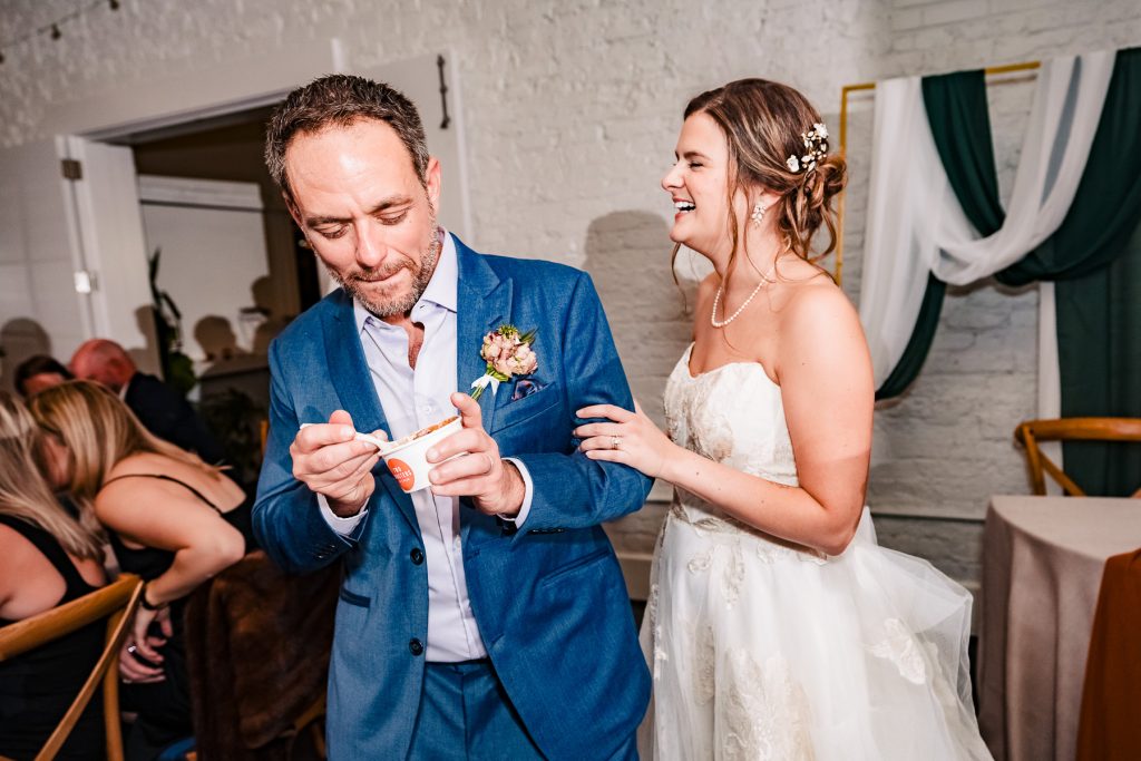 couple in wedding attire laugh as they eat Two Roosters ice cream at their wedding at Junction West in downtown Raleigh