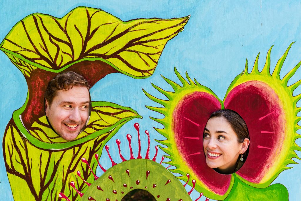 two people put their heads through a painted plywood photo opp so that their faces are in the center of a venus fly trap and a pitcher plant