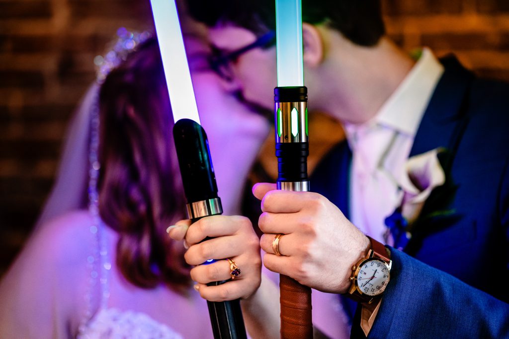 Couple holds lightsabers and shows off their wedding rings at their Olde Raleigh Distillery wedding