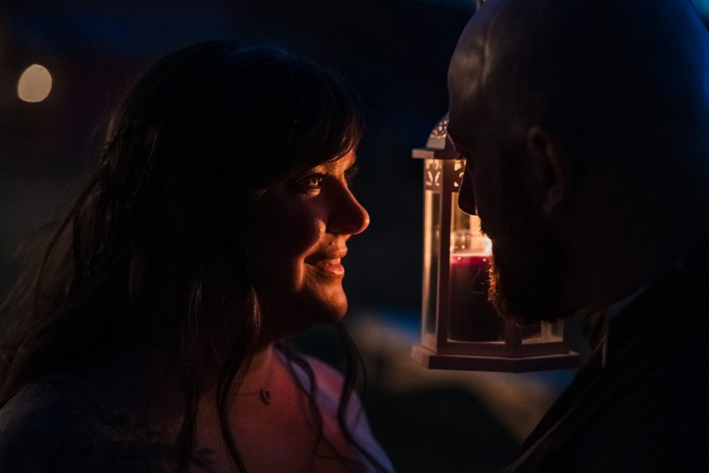 man holds a lantern up, lighting woman's face with candle light