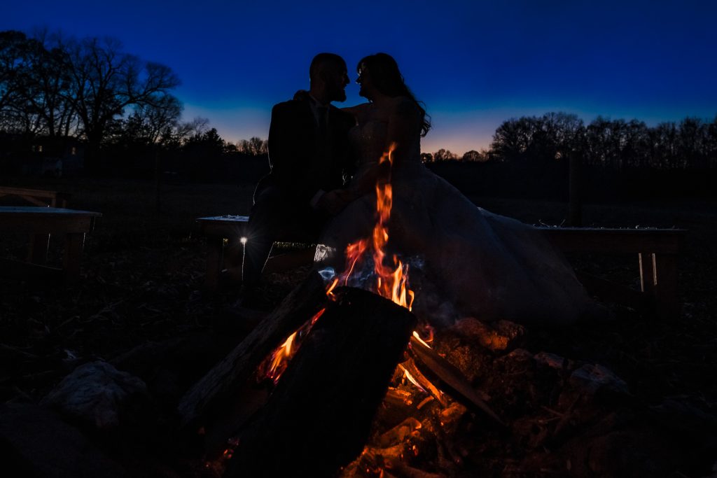 Silhouette of two people looking at each other, with a fire pit in the foreground