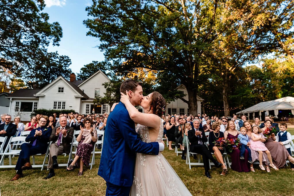 bride and groom share their first kiss - their guests applaud in the background