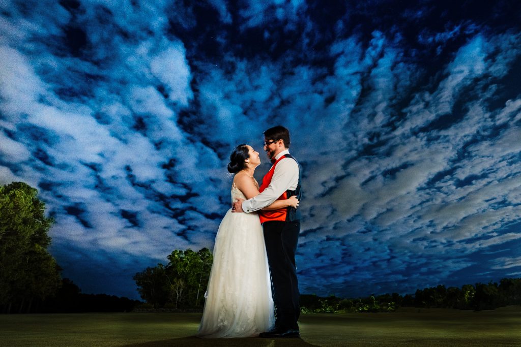 bride and groom pose for a long exposure portrait with clouds moving above. | photo by Kivus & Camera
