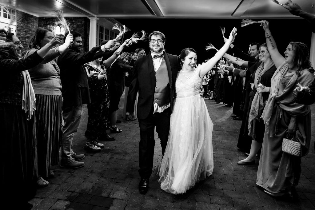 black and white photo of a bride and groom leaving their wedding through a tunnel of their friends and family | photo by Kivus & Camera