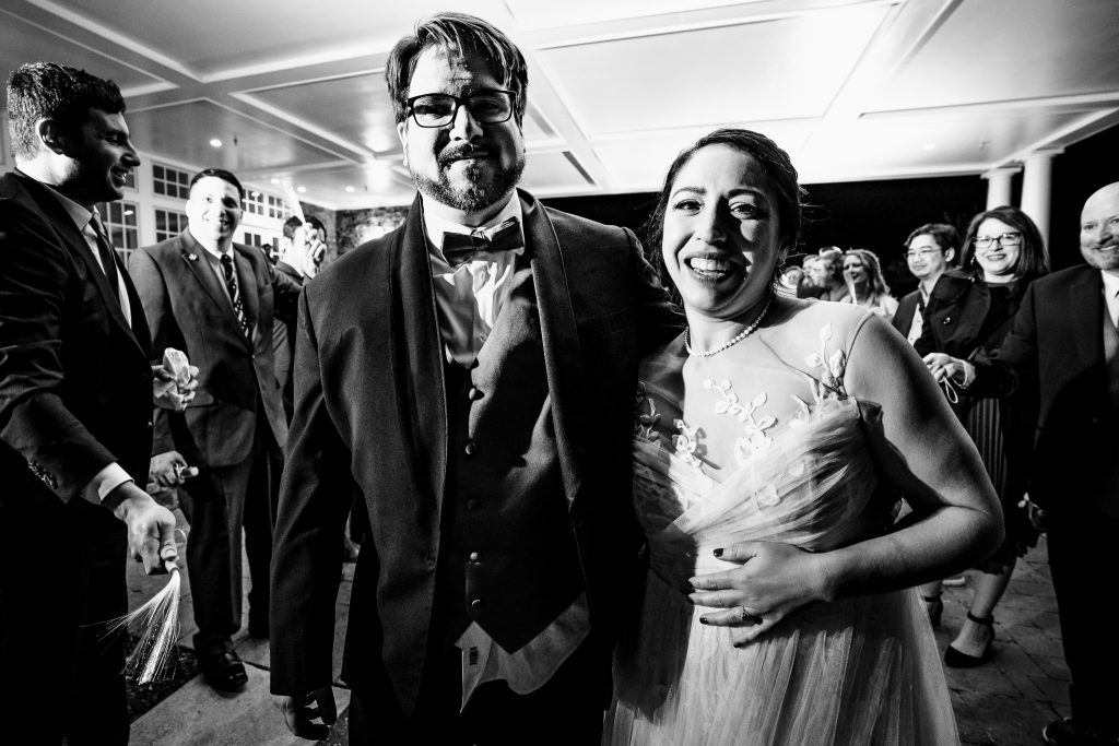 black and white photo of a bride and groom leaving their wedding through a tunnel of their friends and family | photo by Kivus & Camera