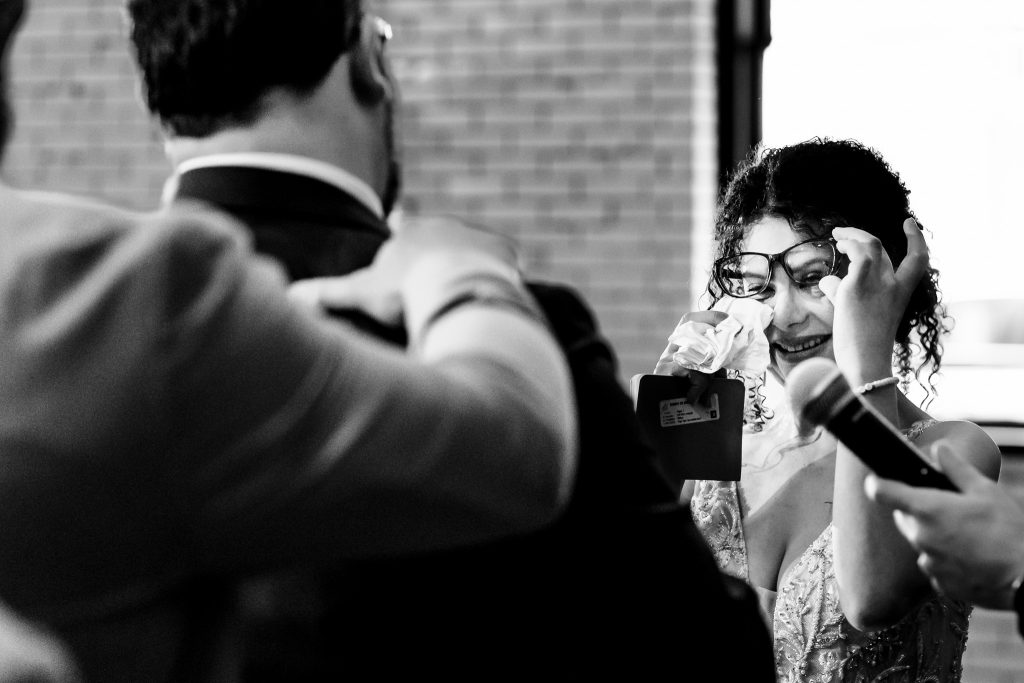 bride lifts her glasses to wipe tears with a tissue during groom's vows at their wedding ceremony