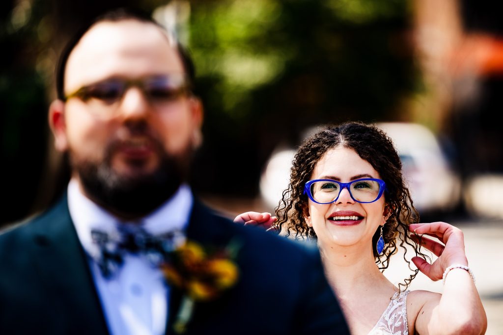 bride wearing bright blue glasses walks up behind groom