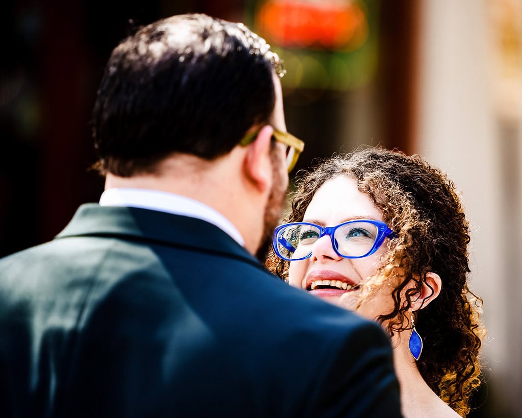 bride in bright blue glasses reacts with a wide smile as she sees the groom for the first time on their wedding day