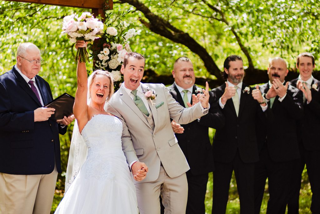 bride and groom celebrate at the end of their wedding ceremony with their hands up in the air