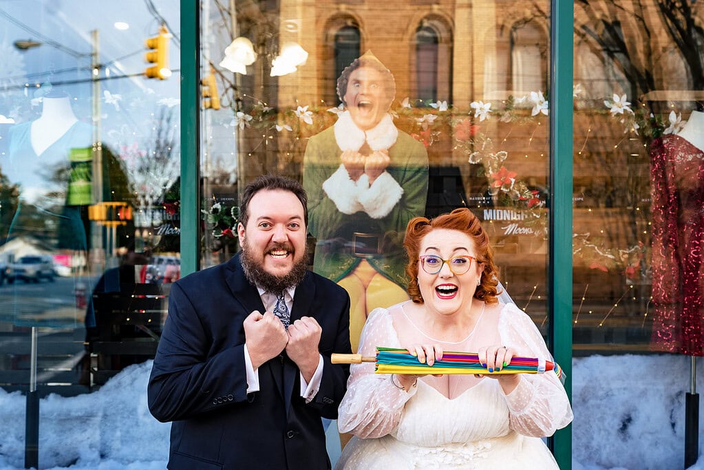 Couple in wedding attire poses in front of a cardboard cutout of Will Ferrell in the movie Elf during their winter wedding in North Carolina | photo by Kivus & Camera