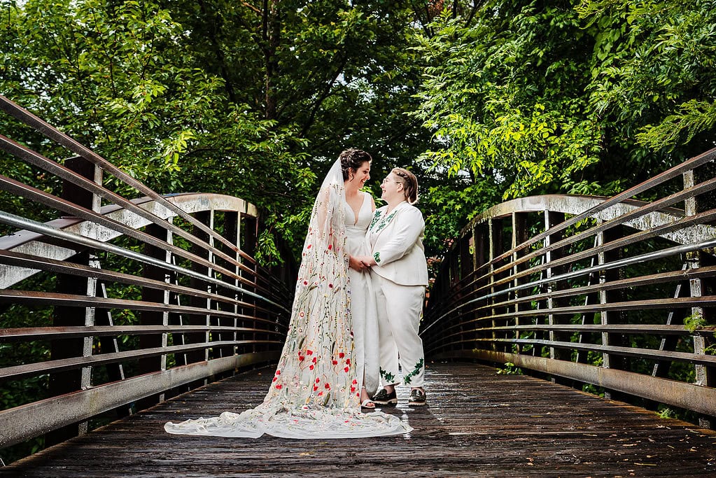 two women, one in a white suit and one in a white dress pose for a portrait on their wedding day at Durham Central Park in Durham, North Carolina | photo by Kivus & Camera