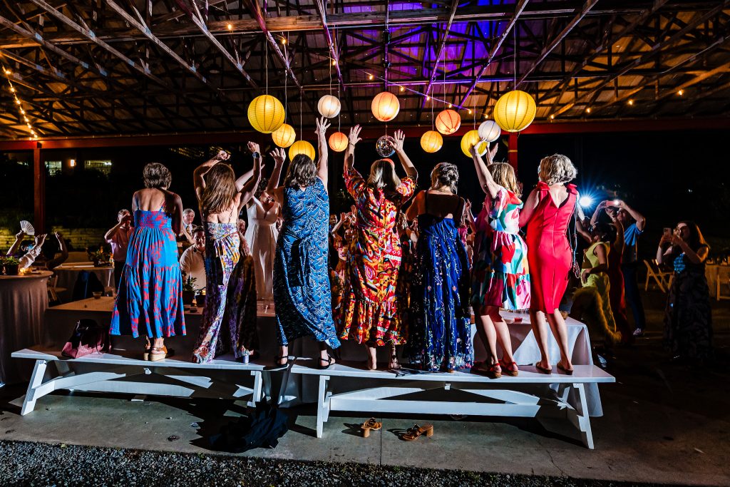 Women in dresses standing on a bench during a wedding reception | photo by Kivus & Camera