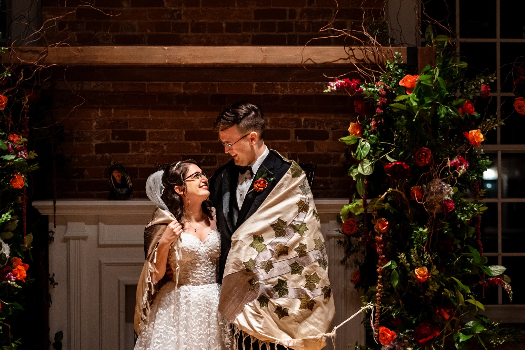 Jewish wedding couple look at one another while wrapped in their custom wedding tallit | photo by Kivus & Camera