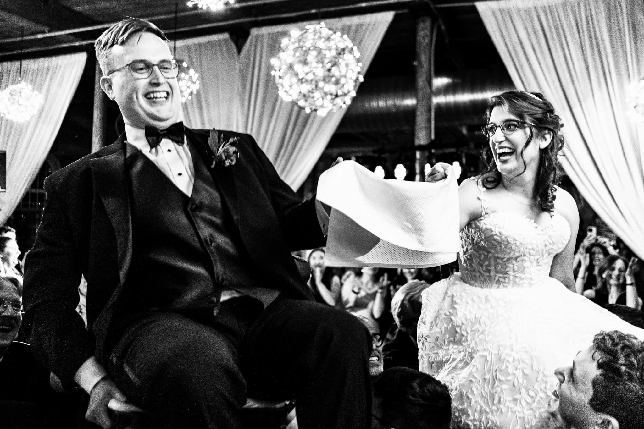 black and white photo of a couple lifted into the air during the hora at their wedding | photo by Kivus & Camera
